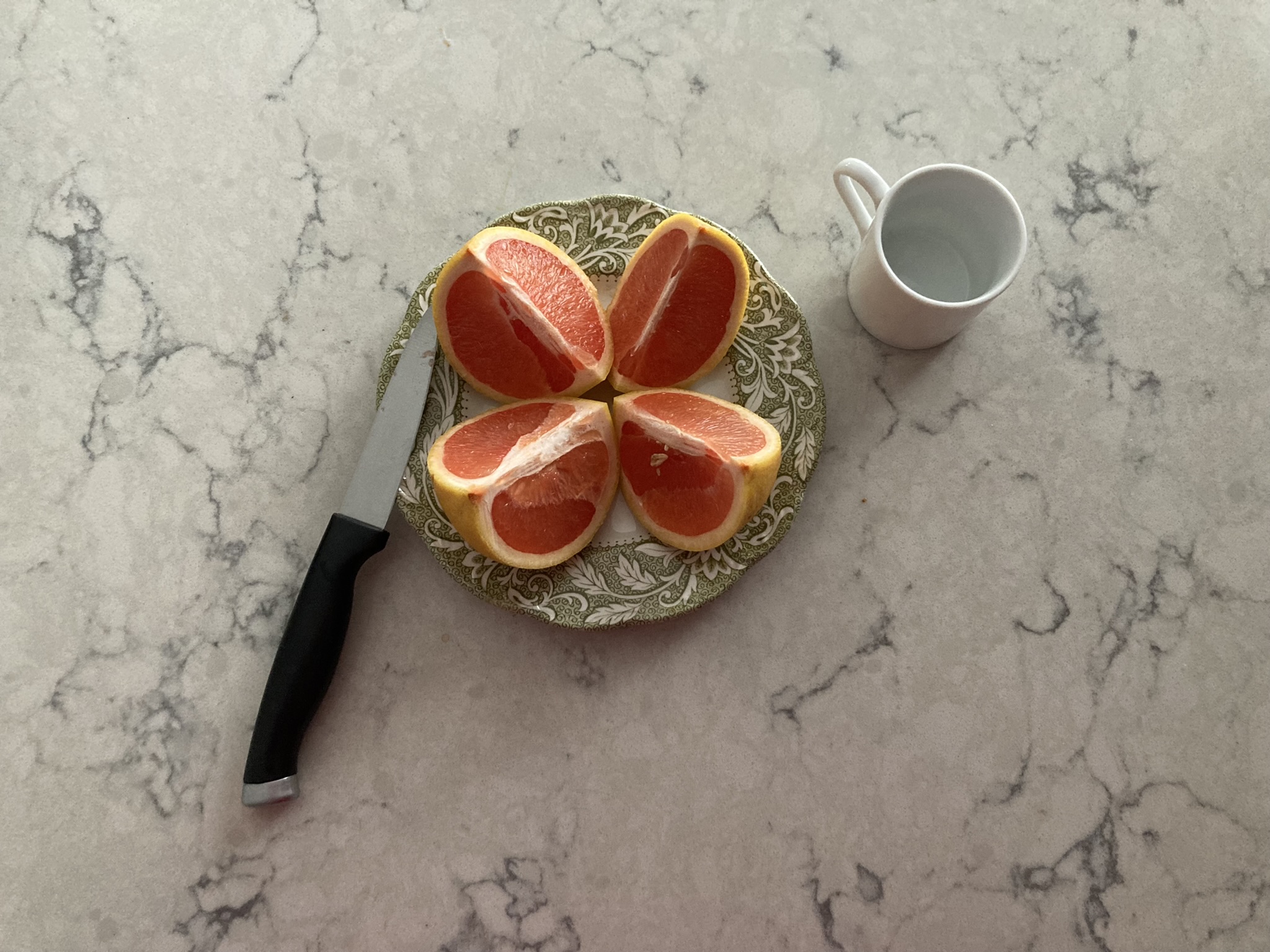 the knife & the grapefruit quartered vertically on the plate with the raised lip