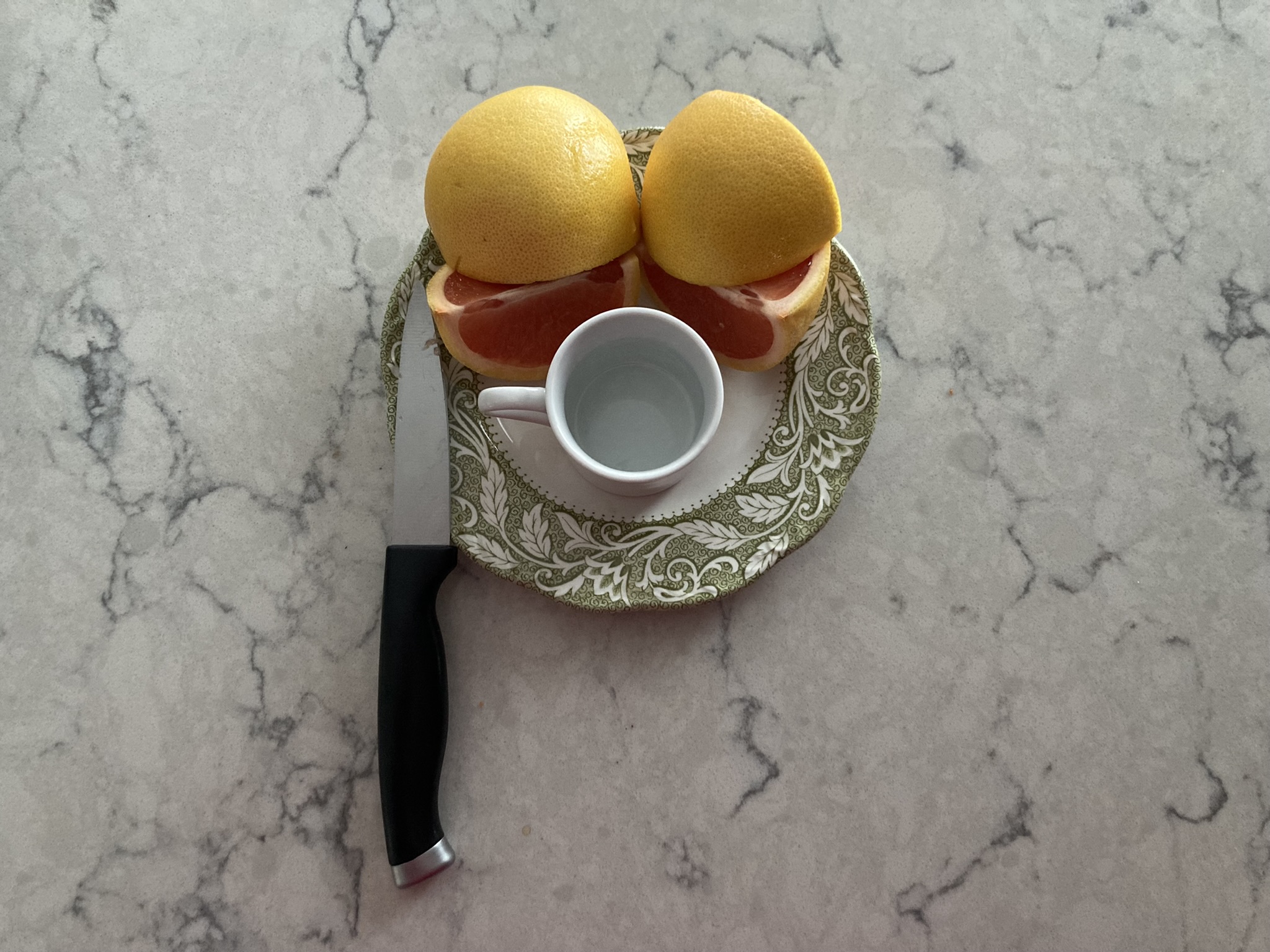 the knife & the grapefruit & the little cup together on the plate with the raised lip