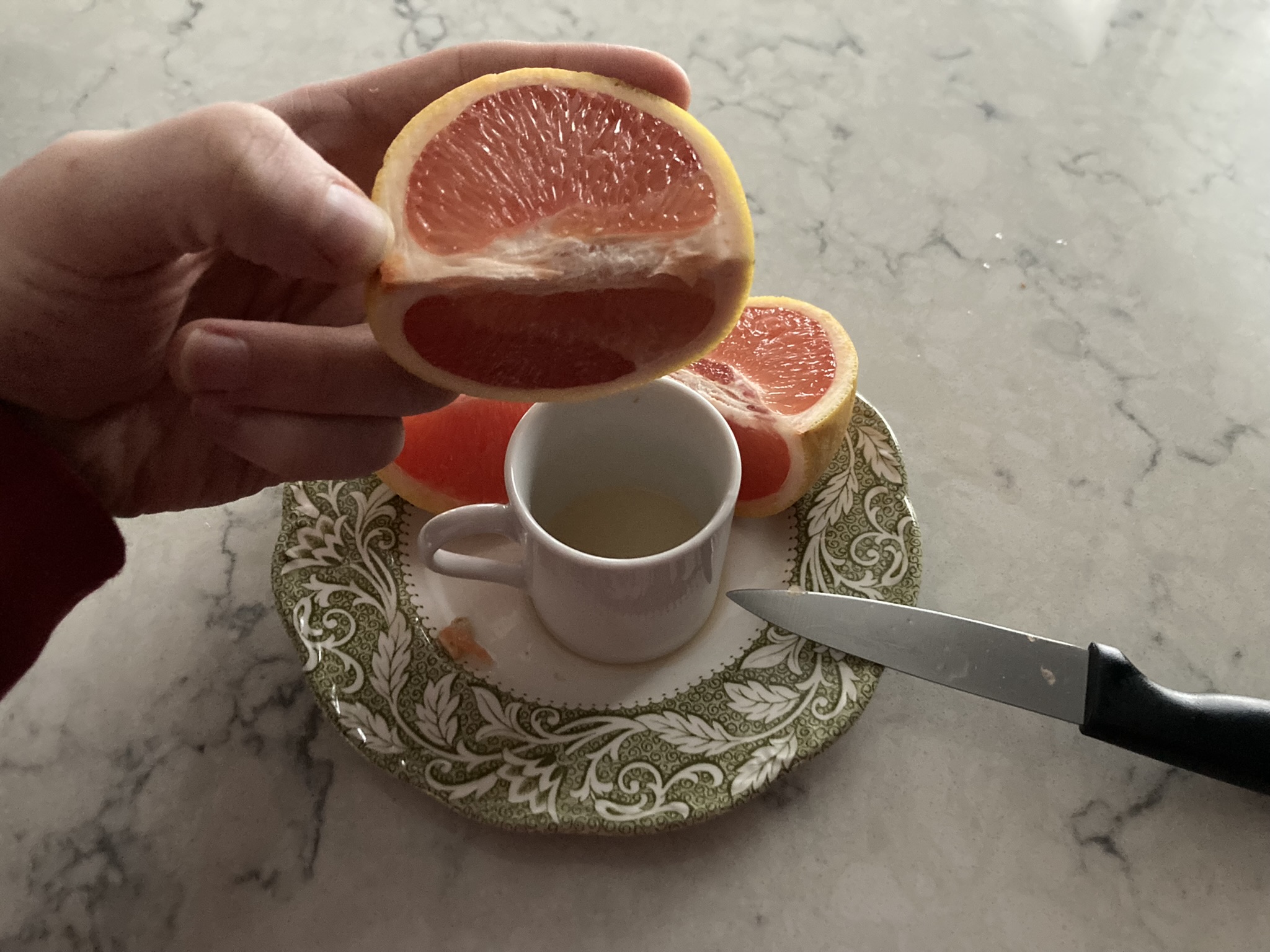 holding one quarter of the grapefruit horizontally above the little cup