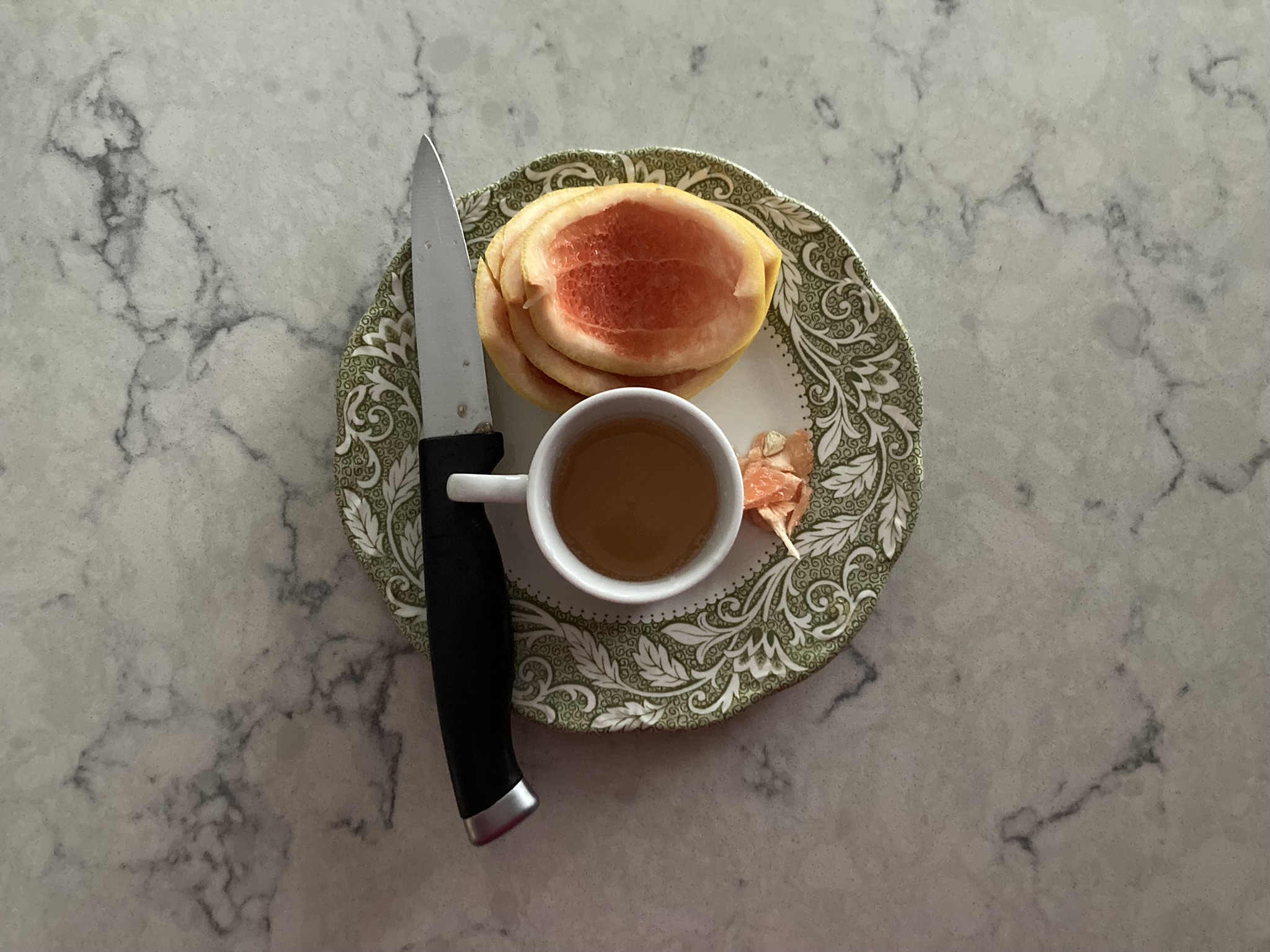 the knife, the excarpated grapefruit, & the cordial of the little cup on the plate with the raised lip